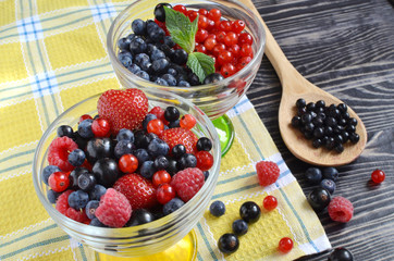 berries are red and blue in a glass bowl on a black wooden background