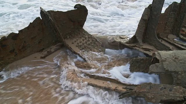 Close up of a ship wrecks hull on the beach surrounded by calm waves