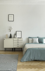 Real photo of bright bedroom interior with striped carpet on herringbone parquet, pastel bedding on...