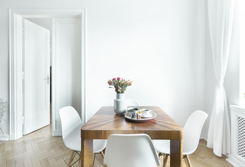 Dining table with fresh flowers and breakfast tray with coffee cup and fruits in real photo of...