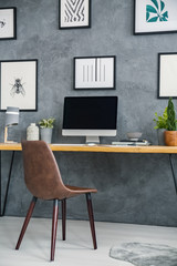 Simple desk with a computer and plant, paintings on the wall and brown chair in a home office interior. Place your product