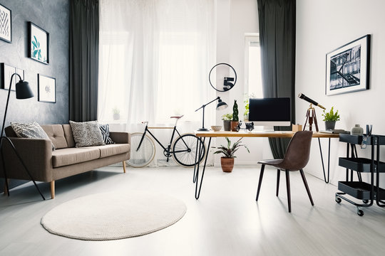Modern home office interior with a big window, sofa, bike and desk with a computer. Place your product