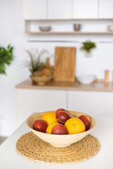 close up view of oranges and plums in bowl at kitchen table