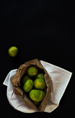 Overhead view of a recycled paper bag with organic fig fruits on unpolluted white fabric. Dark still life scene with black and elegant background.