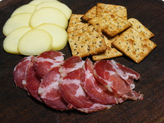 Wooden plate with cheese, ham and crackers.