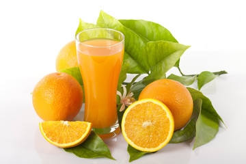 Oranges and orange tree leaves next to a glass full of orange juice isolated