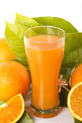 Oranges and orange tree leaves next to a glass full of orange juice isolated