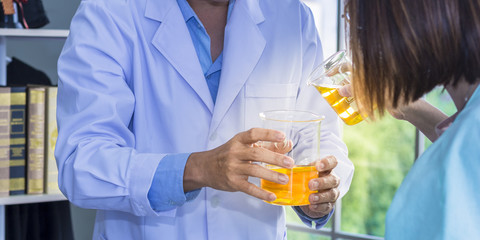 Senior male scientist and student mixing bright orange substances in glassware.Copy space.