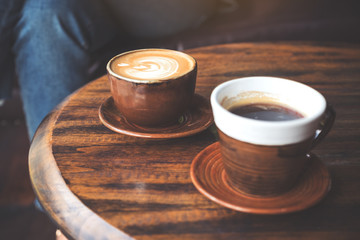 Closeup image of two cups of hot latte coffee and black coffee on vintage wooden table in cafe