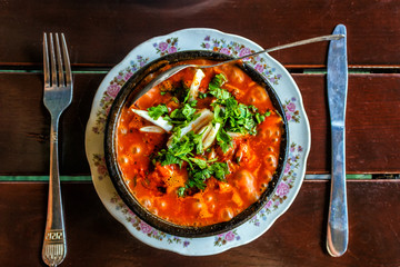 Shashushuli traditional homemade Georgian meat dish with vegetables with spicy sauce in a cast-iron pan frying pan on the background of a wooden table.