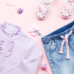 Little girl clothes collection flat lay with cardigan, jeans, sandals on pink background.