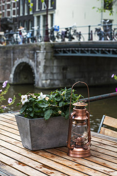 One small copper lantern is on the wooden table with flowers near the river in the day