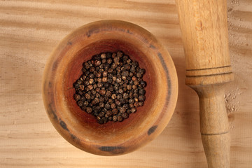 An overhead closeup photo of black peppercorns in a mortar with a pestle