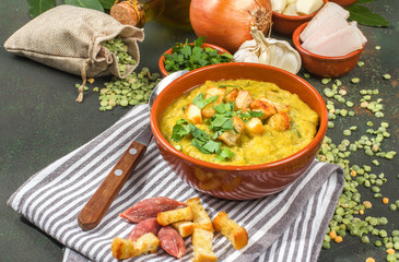Split pea soup in rustic bowl decorated with fresh green leaves, garlic, onion and slices of lard