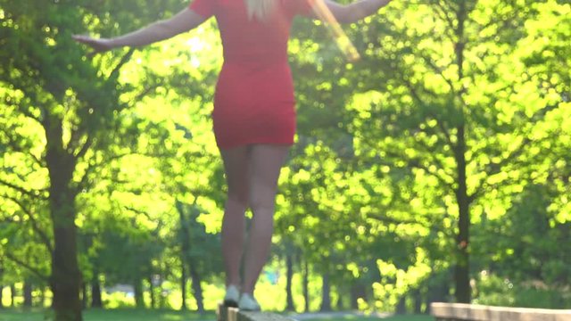 A woman in a red dress walks along a wooden railing in a park on a sunny day