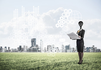 Camera headed woman standing on green grass against modern citys