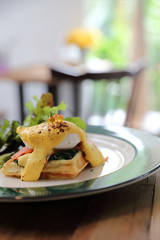 Breakfast food egg benedict , poached egg with yellow sauce with waffle and smoked salmon on wood background