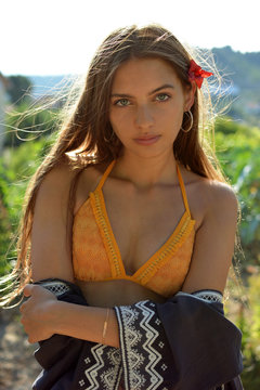 mujer  joven atractiva con rasgos latinos  de mirada penetrante, bonitos labios y pelo largo vistiendo  bikini naranja en flor en el cabello y fondo exterior con arboles