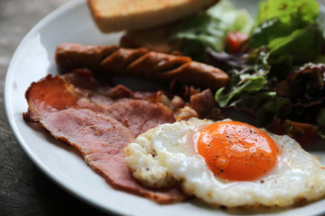 English breakfast  fried egg, ham,sausage, bacon,salad and toast on wood background in mystic light