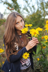 A beautiful teenage girl walks in the fall in the garden and smells fall yellow flowers