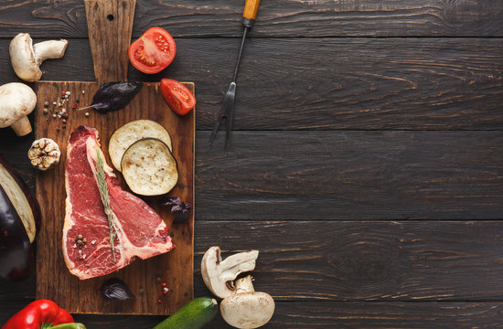 Raw t-bone steak with vegetables on wooden board