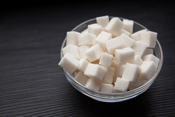 White sugar cubes in round bowl on black background with copy space, food ingredient