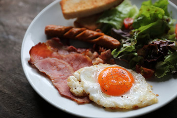 English breakfast  fried egg, ham,sausage, bacon,salad and toast on wood background in mystic light