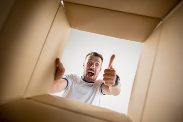 The surprised man unpacking, opening carton box and looking inside. The package, delivery,...