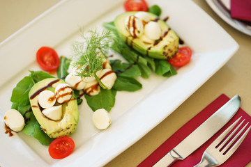 Avocado salad with mozzarella cheese, cherry tomatoes, herbs and sauce in a plate on the table in a restaurant.