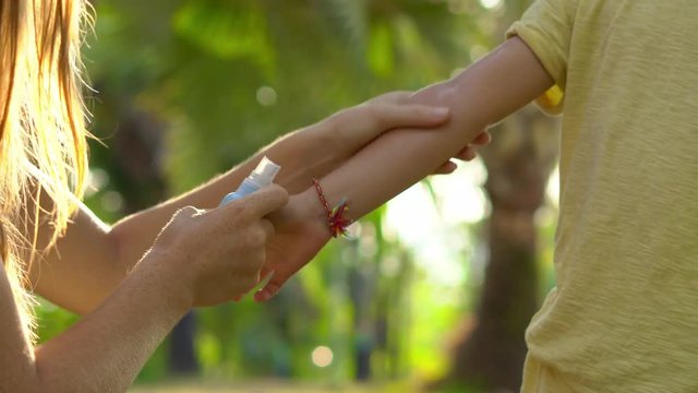 Young woman in a tropical park puts a mosquito repellent on her son