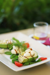 Avocado salad with mozzarella cheese, cherry tomatoes, herbs and sauce in a plate on the table in a restaurant.