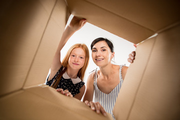 The surprised mom and daughter unpacking, opening carton box and looking inside. The package,...