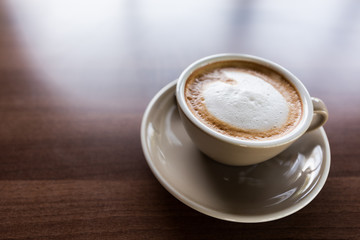 Cappuccino coffee cup on wooden table near windows