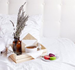 Morning breakfast in bed wooden tray with a cup of tea, sweet colorful french macaroons, love letter, bouquet of lavender. Top view Morning at Hotel or at home. Background Concept Cozy morning