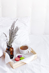 Morning breakfast in bed wooden tray with a cup of tea, sweet colorful french macaroons, love letter, bouquet of lavender. Top view Morning at Hotel or at home. Background Concept Cozy morning