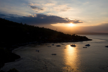 Amazing beach sunset with boats silhouettes. Volcanic hills in the background.