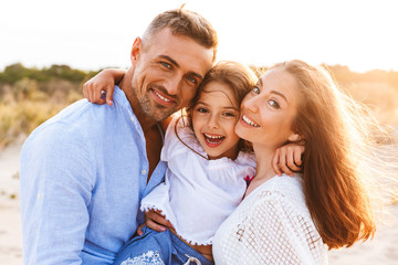 Fototapeta premium Parents having fun together outdoors at the beach with their daughter.