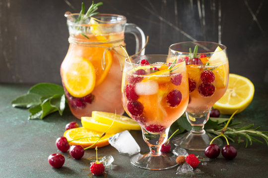 Homemade refreshing wine sangria or punch with fruits in glasses. Sangria cocktails with fresh fruits, berries and rosemary. On a stone or slate background, with a jug and ingredients. Copy space.