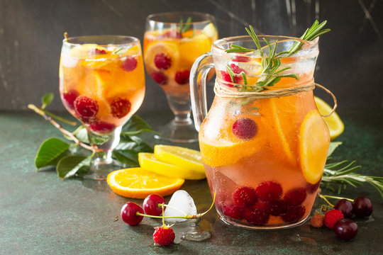 Homemade refreshing wine sangria or punch with fruits in glasses. Sangria cocktails with fresh fruits, berries and rosemary. On a stone or slate background, with a jug and ingredients. Copy space.