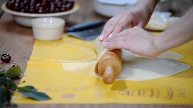 Woman hands roll out the dough on the kitchen table to make a pie with berries.