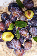 Plums on rustic background. Half of blue plum fruit. Many beautiful plums with leaves