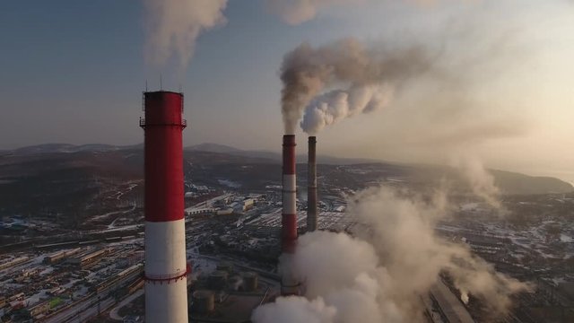 Aerial sideways flight around pipes  of industrial factory. Steam smoke production energy complex profession contamination. City Soviet Vladivostok Russia Asia. Winter snow 