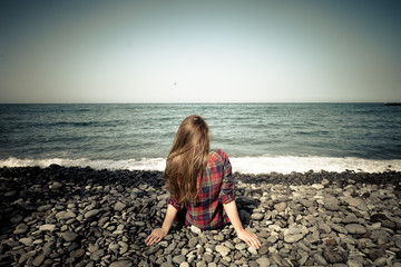 nice girl viewed from rear sit down at the beach and look at the sea. silence and peace feeling in outdoor leisure activity of meditation. enjoy life and see the waves to relax