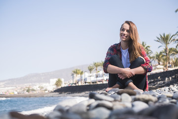 Fototapeta na wymiar young smile beautiful lady sitting on the rocks near the ocean and the waves to enjoy the outdoor leisure activity on summer vacation. beautiful woman with modern casual clothes