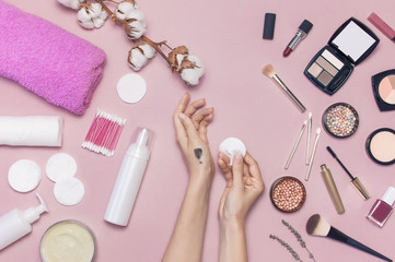 Make-up Remover Accessories. Flat lay background Womens hands try cosmetics, cotton branch, cotton pads, cosmetic bottle containers, pink towel, various make-up cosmetics, mascara, powder, lipstick