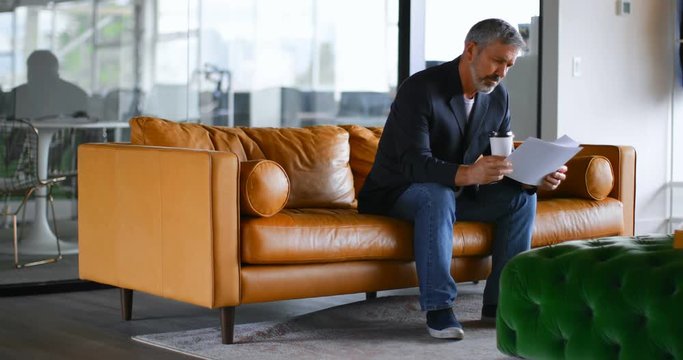 Businessman with coffee cup checking document on sofa 4k