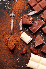 Сhocolate pieces and cocoa powder on marble. The chunks of chocolate over dark background