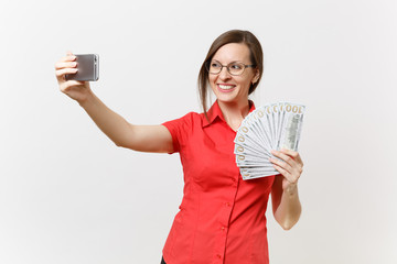 Excited business woman in red shirt doing taking selfie shot on mobile phone with bundle lots of dollars, cash money isolated on white background. Education teaching in high school university concept.