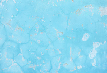 A bright blue wall with cracked paint. Abstract background.