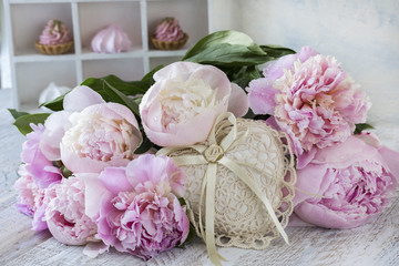 on the table a bouquet of pink peonies, a heart of lace and pink cakes and meringues